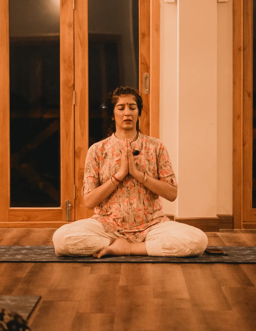 A teacher seated in prayer pose in the meditation hall