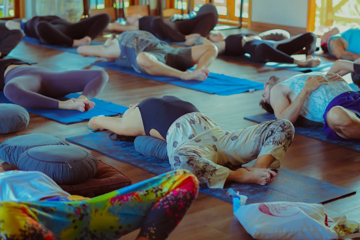 Students resting in a supported reclining pose on mats in the yoga hall
