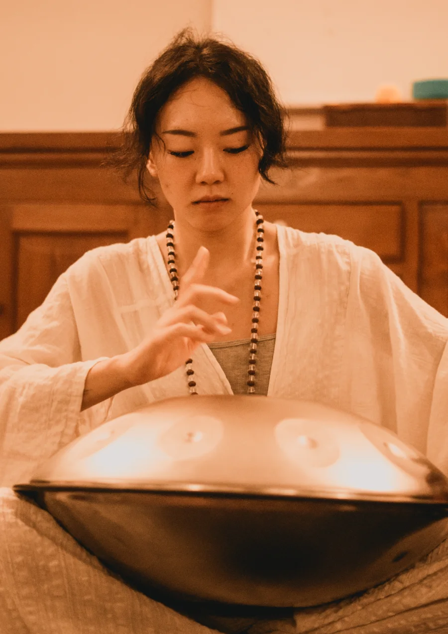 A student playing the handpan with eyes lowered in meditation