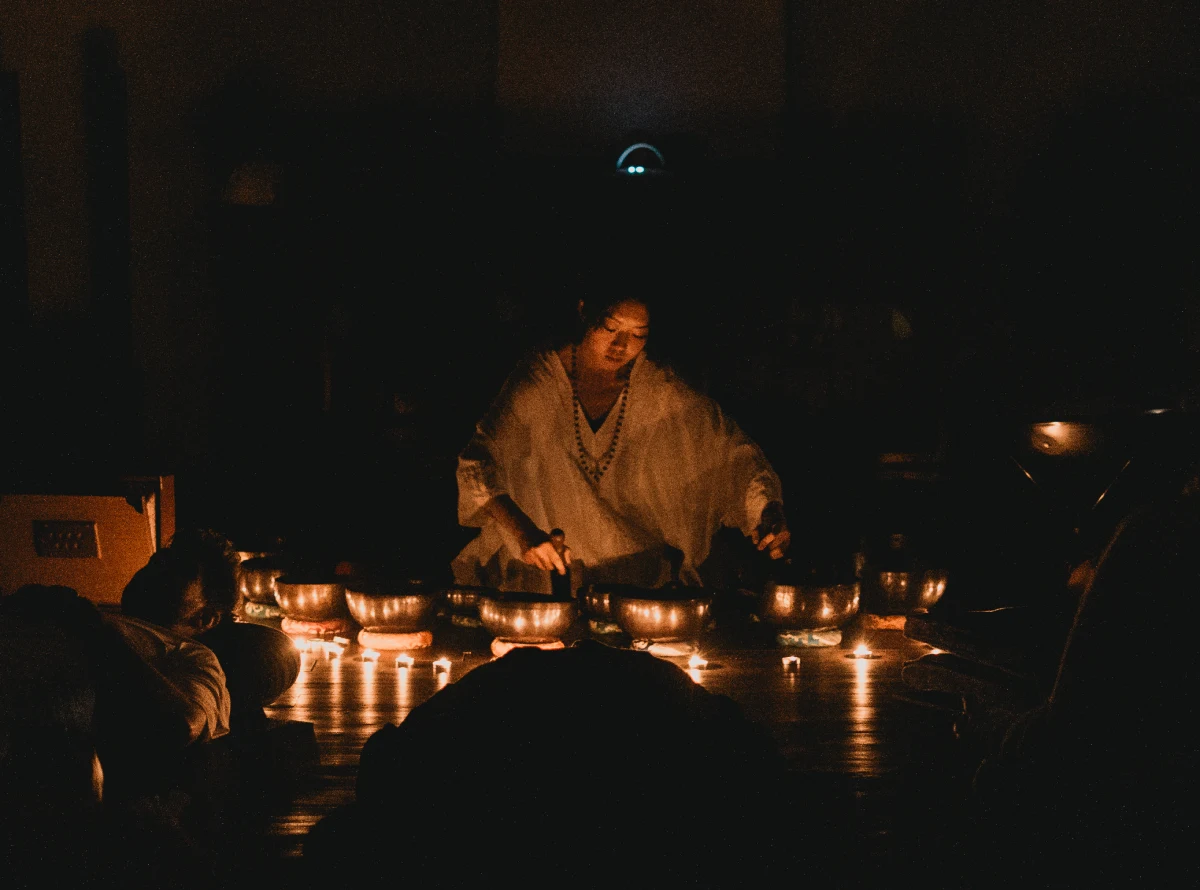 A teacher playing singing bowls by candlelight during a sound bath