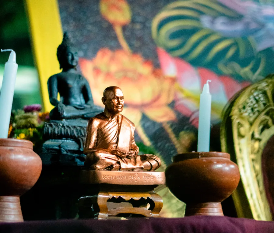 A bronze statue of a meditating monk between candles on a Thai shrine