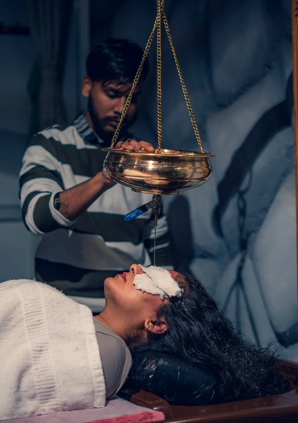 A therapist preparing Shirodhara with a brass oil vessel