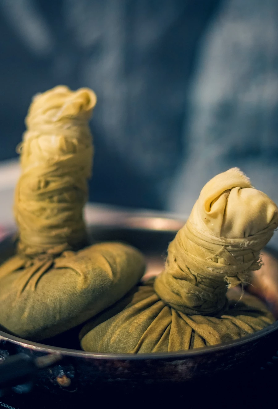 Herbal Kizhi poultices warming in a pan