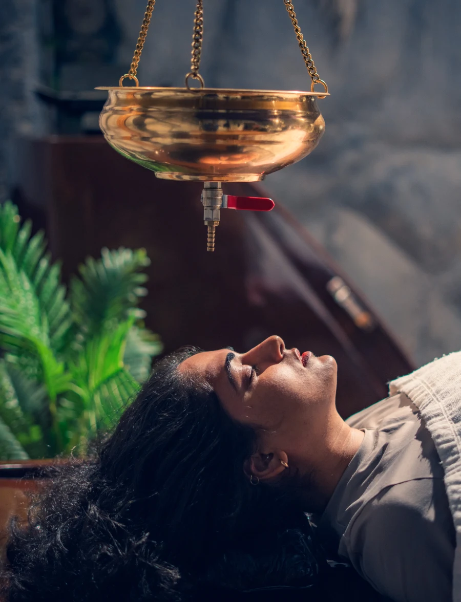 A guest resting under the brass Shirodhara vessel